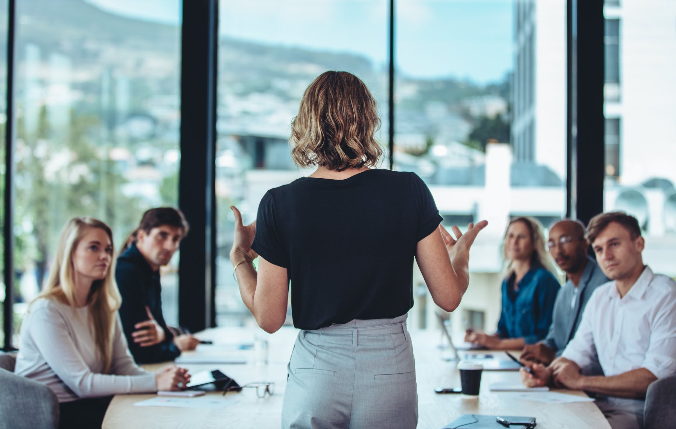 Rear view of a woman explaining new strategies to coworkers during conference meeting in office. Businesspeople meeting in office board room for new project discussion.